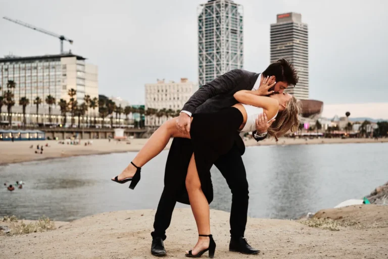 Romantic dip-kiss on the beach walkway featuring the iconic Barcelona skyline at twilight.