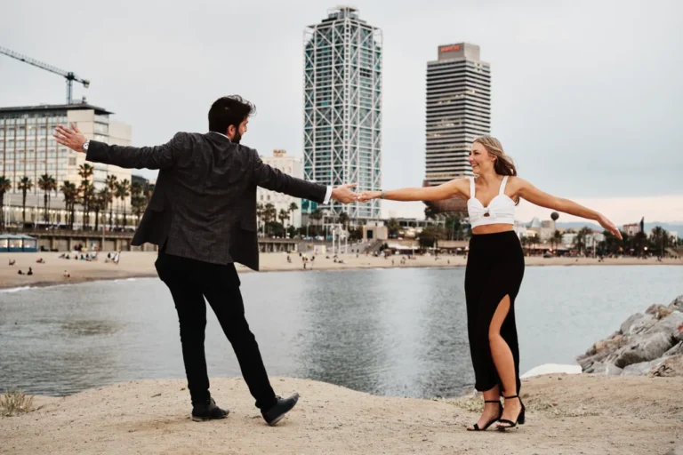 Romantic couple embrace on the Barceloneta promenade with palm trees and the Mediterranean sea.