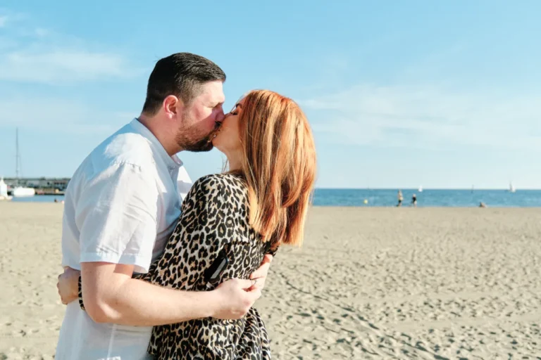 Romantic couple sharing a kiss on the sand with the blue Mediterranean Sea as a backdrop.