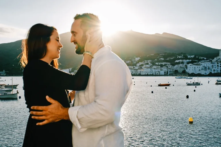 Romantic couple embrace on a seaside balcony overlooking the white village of Cadaqués.
