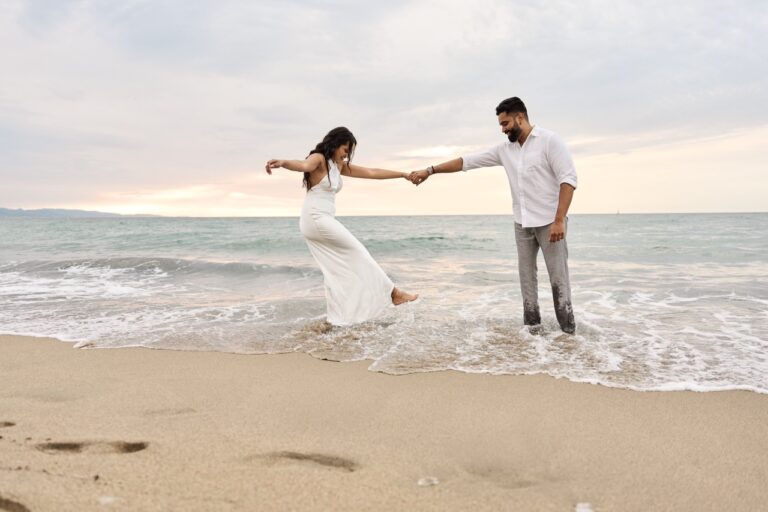 Engaged couple walking hand-in-hand through the waves on a Barcelona beach, a perfect end to a surprise proposal.