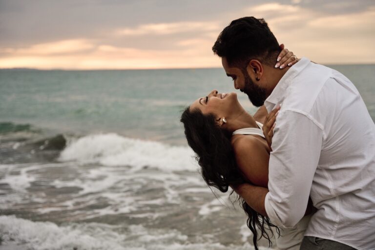Emotional kiss between a newly engaged couple on the shoreline during a professional photo session.