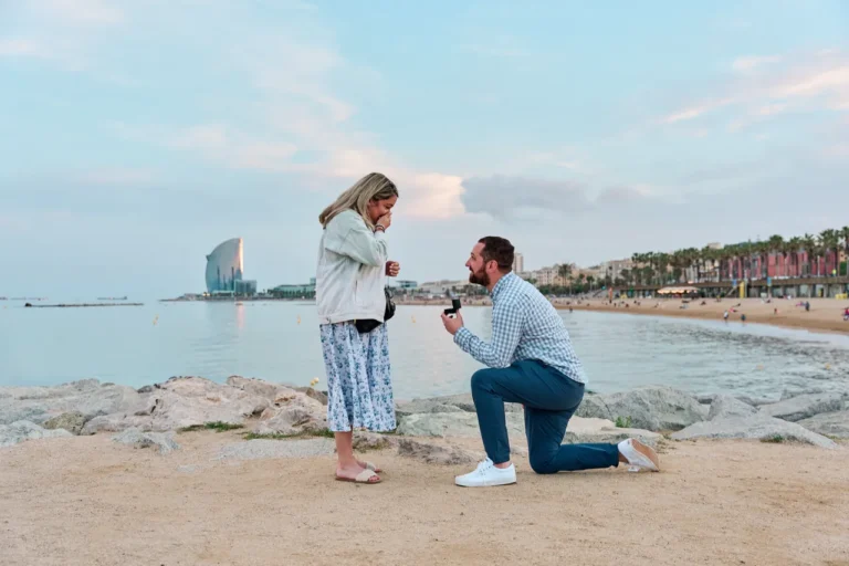 Romantic marriage proposal on the rocky shore of Barceloneta Beach with the W Hotel in the distance.