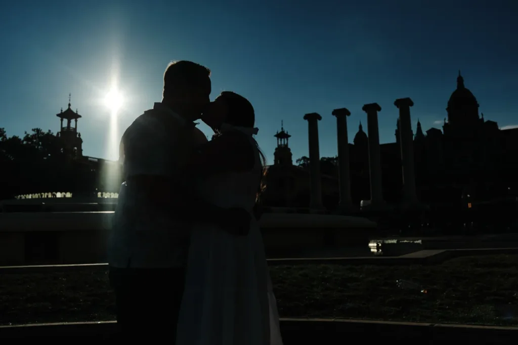 Cinematic silhouette of a couple kissing against the sunset at the Montjuïc columns.