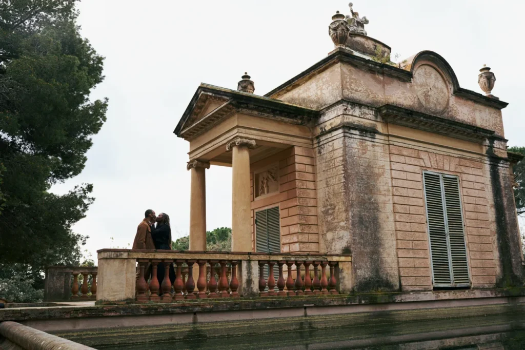 Couple embracing in front of the neoclassical pavilion and statues at the Horta Labyrinth Park.