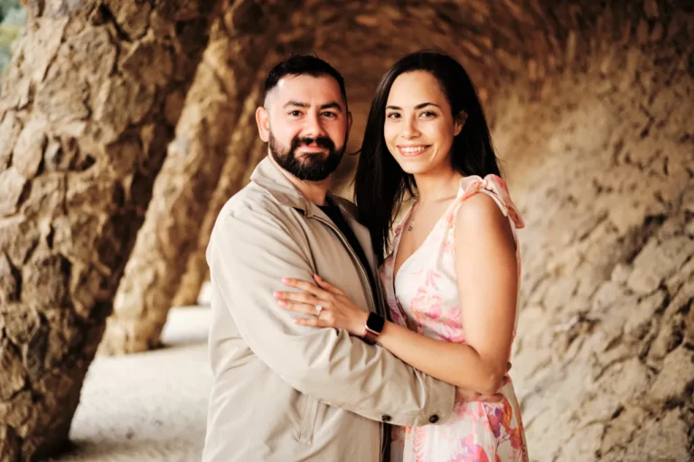 Romantic couple portrait framed by the rustic stone pillars of Gaudí's Park Güell.