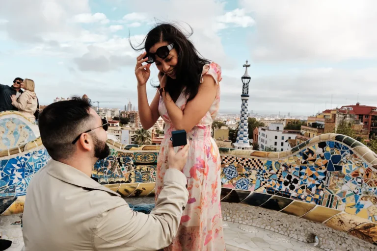 Newly engaged couple embracing with the gingerbread-style houses of Park Güell in the background.