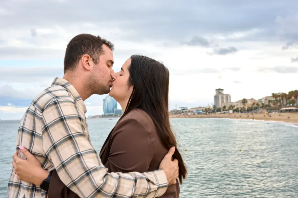 Romantic couple kissing by the Mediterranean Sea after a surprise beach proposal.