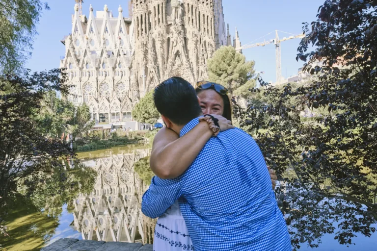 Newly engaged couple sharing a joyful hug in front of the Sagrada Família lake.