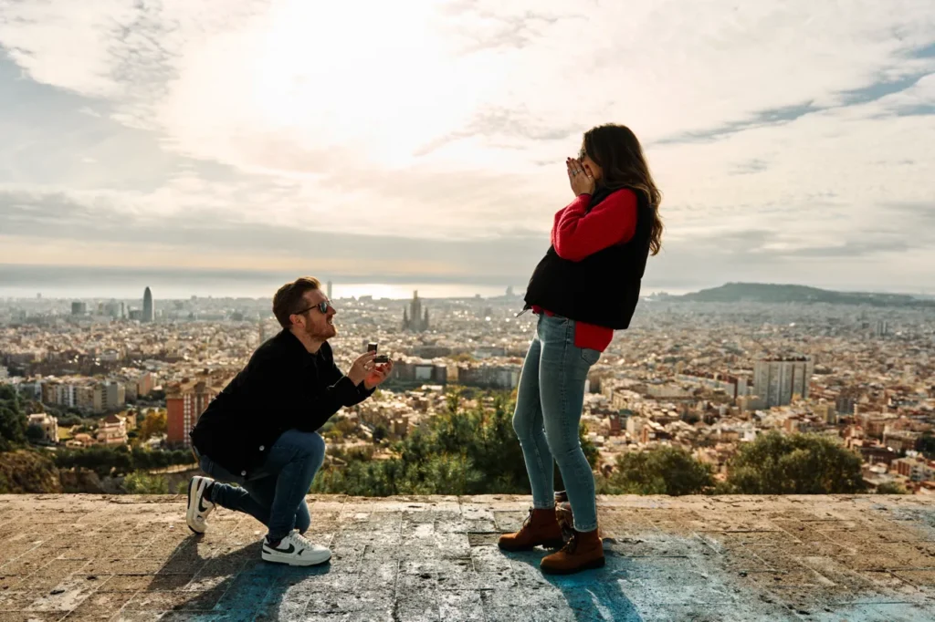Man kneeling for a surprise proposal with the Barcelona skyline in the background.