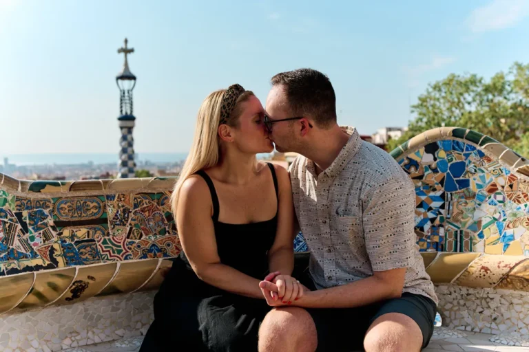Romantic couple sharing a kiss on the mosaic benches of Park Güell.