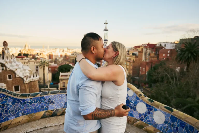 Couple embracing at Park Güell with Gaudi’s colorful mosaics and Barcelona views.